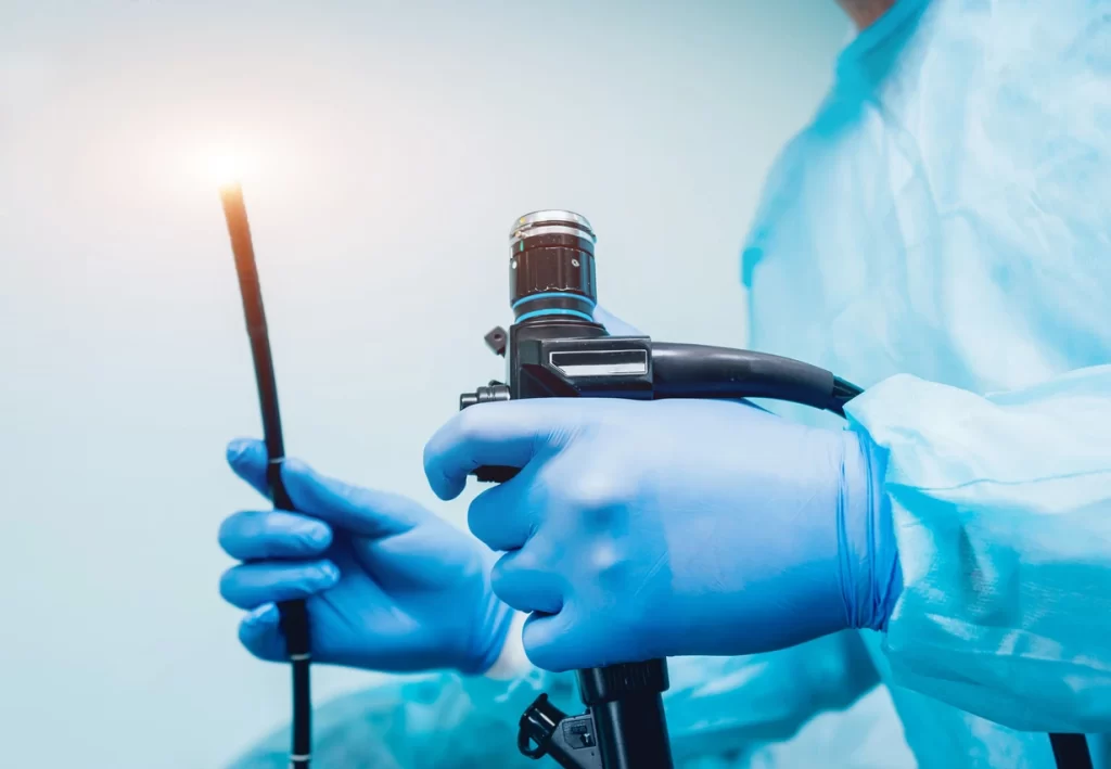 Gloved medical professional holding an endoscope with illuminated tip during a diagnostic procedure.
